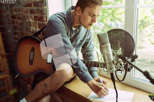 Image of Young man recording music, playing guitar and singing at home