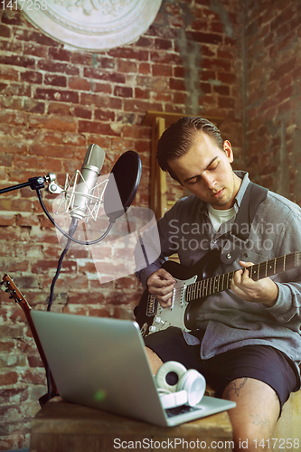 Image of Young man recording music, playing guitar and singing at home