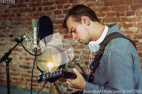 Image of Young man recording music, playing guitar and singing at home