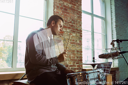 Image of Young man recording music, playing drums and singing at home