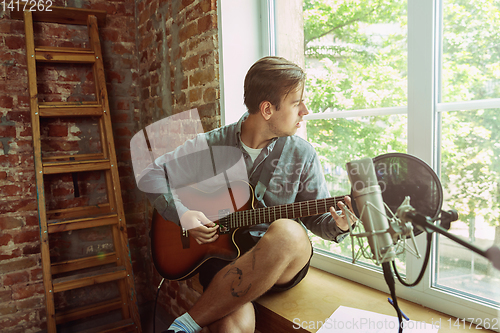 Image of Young man recording music, playing guitar and singing at home