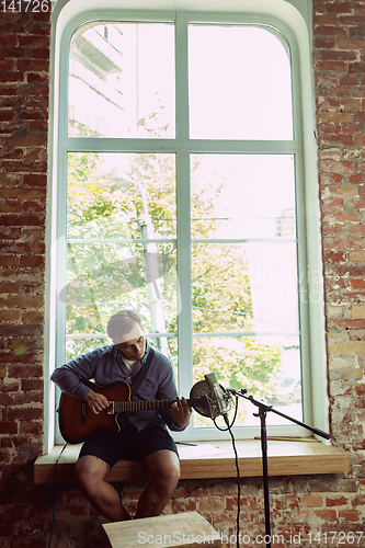 Image of Young man recording music, playing guitar and singing at home