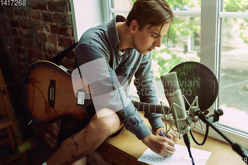 Image of Young man recording music, playing guitar and singing at home