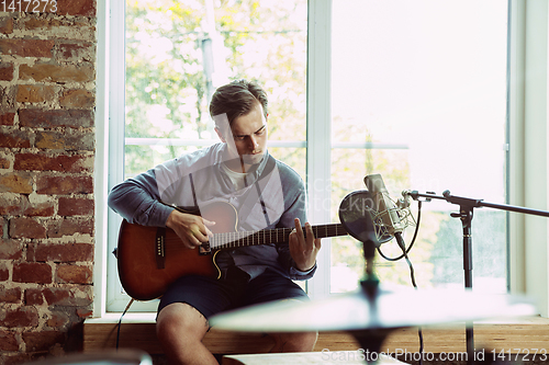 Image of Young man recording music, playing guitar and singing at home