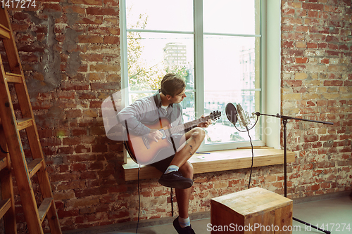 Image of Young man recording music, playing guitar and singing at home