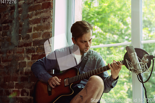 Image of Young man recording music, playing guitar and singing at home
