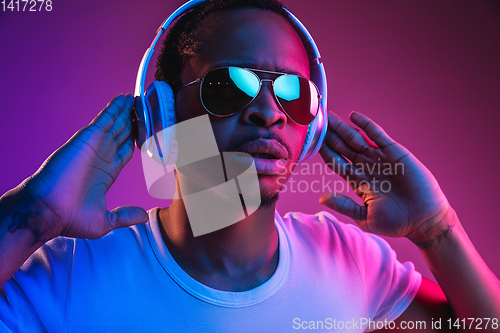 Image of Young african-american man\'s listening to music in neon light