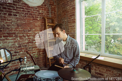 Image of Young man recording music, playing drums and singing at home