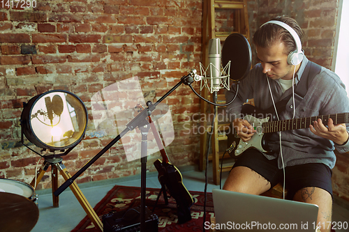 Image of Young man recording music, playing guitar and singing at home