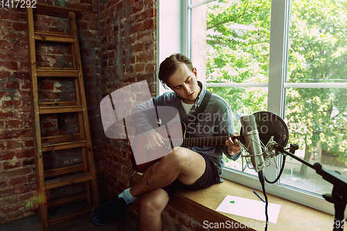 Image of Young man recording music, playing guitar and singing at home