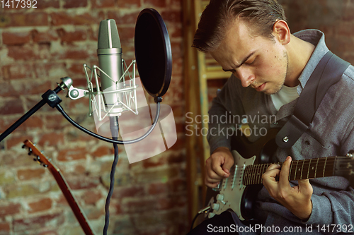 Image of Young man recording music, playing guitar and singing at home