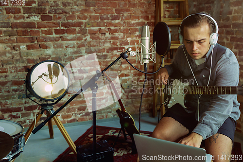 Image of Young man recording music, playing guitar and singing at home