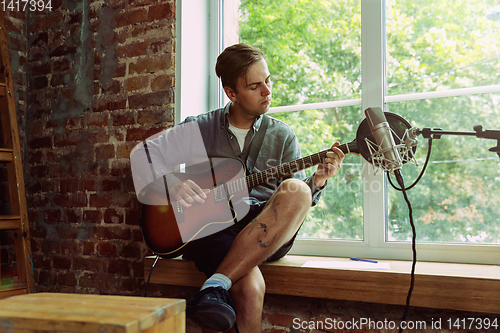 Image of Young man recording music, playing guitar and singing at home