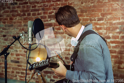 Image of Young man recording music, playing guitar and singing at home