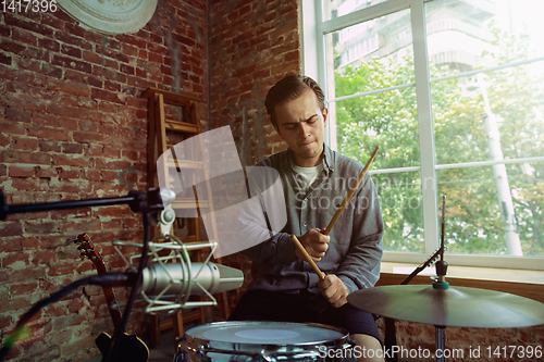 Image of Young man recording music, playing drums and singing at home