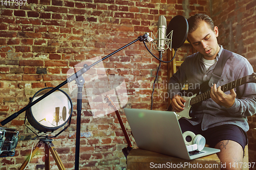 Image of Young man recording music, playing guitar and singing at home