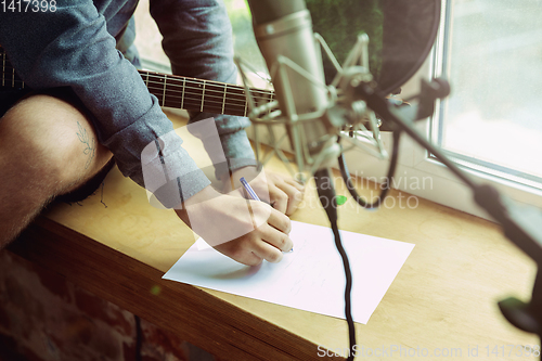 Image of Young man recording music, playing guitar and singing at home