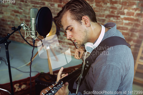 Image of Young man recording music, playing guitar and singing at home