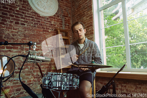 Image of Young man recording music, playing drums and singing at home