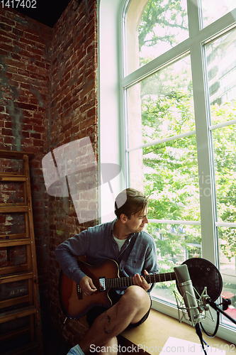 Image of Young man recording music, playing guitar and singing at home