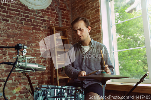 Image of Young man recording music, playing drums and singing at home