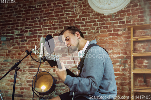 Image of Young man recording music, playing guitar and singing at home