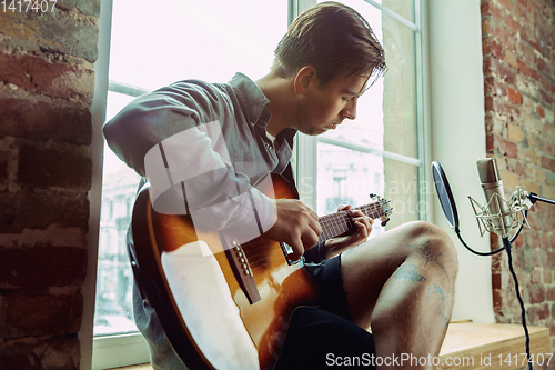 Image of Young man recording music, playing guitar and singing at home