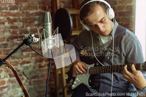 Image of Young man recording music, playing guitar and singing at home