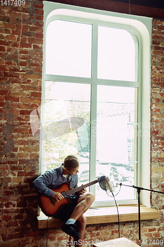 Image of Young man recording music, playing guitar and singing at home