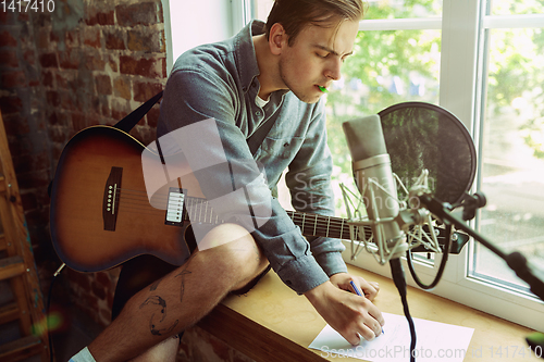 Image of Young man recording music, playing guitar and singing at home