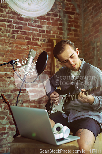 Image of Young man recording music, playing guitar and singing at home