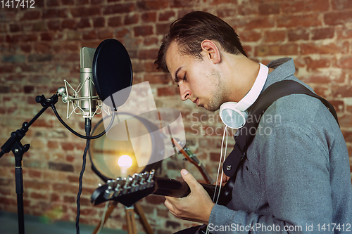 Image of Young man recording music, playing guitar and singing at home