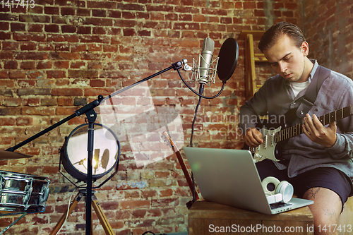 Image of Young man recording music, playing guitar and singing at home