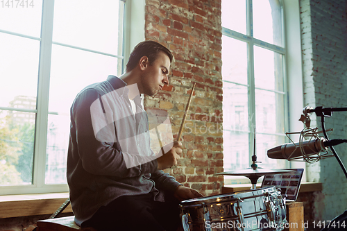 Image of Young man recording music, playing drums and singing at home