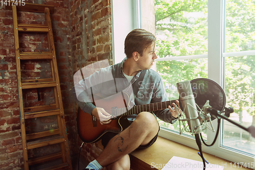 Image of Young man recording music, playing guitar and singing at home