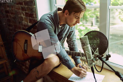 Image of Young man recording music, playing guitar and singing at home