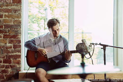 Image of Young man recording music, playing guitar and singing at home