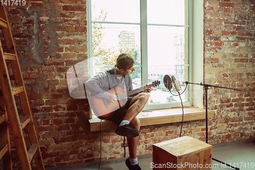 Image of Young man recording music, playing guitar and singing at home