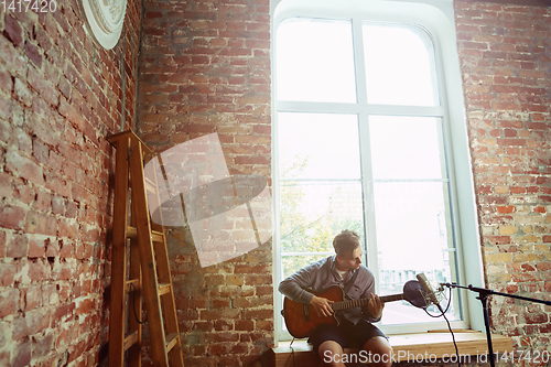 Image of Young man recording music, playing guitar and singing at home