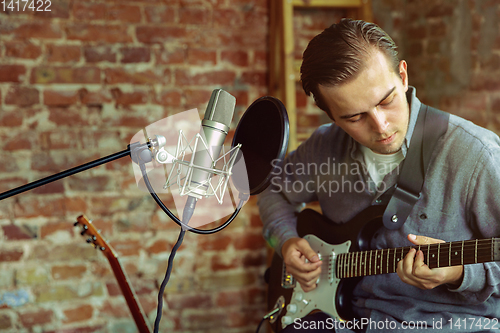 Image of Young man recording music, playing guitar and singing at home