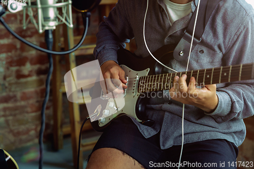 Image of Young man recording music, playing guitar and singing at home