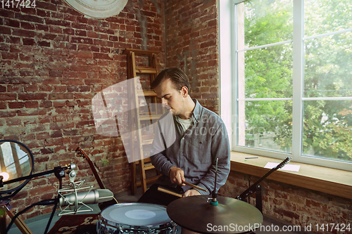 Image of Young man recording music, playing drums and singing at home