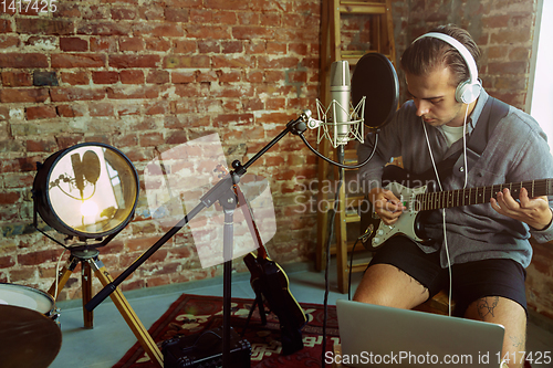 Image of Young man recording music, playing guitar and singing at home