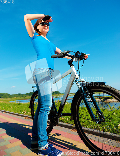 Image of Young woman is standing in front of her bicycle