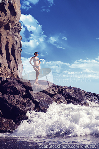 Image of beautiful girl standing on rocky shore