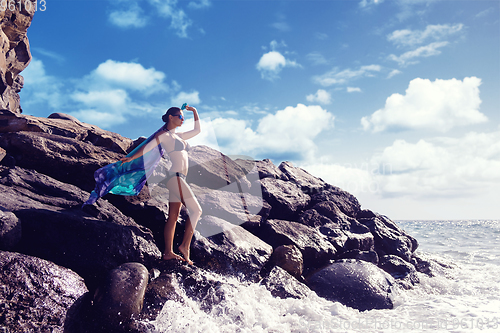 Image of beautiful girl standing on rocky shore