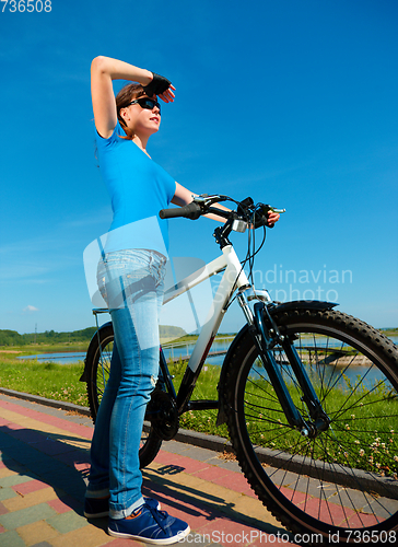 Image of Young woman is standing in front of her bicycle
