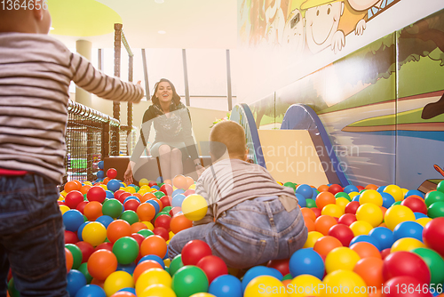 Image of young mom playing with kids in pool with colorful balls