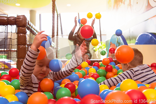 Image of young mom playing with kids in pool with colorful balls