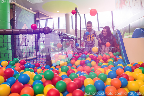 Image of young mom playing with kids in pool with colorful balls